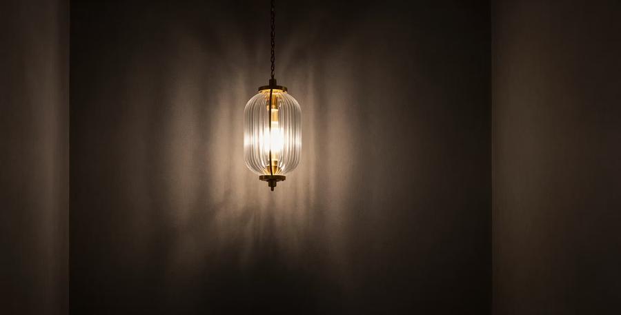 Ribbed glass pendant lantern glowing against a dark wall